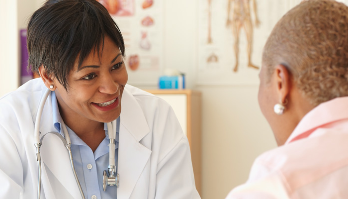 A doctor smiling and talking with a patient in the foreground.