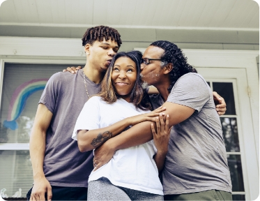 A family with a son and father kissing the mother on the cheek.