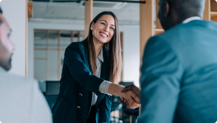 A professional woman shaking hands with someone in the foreground.